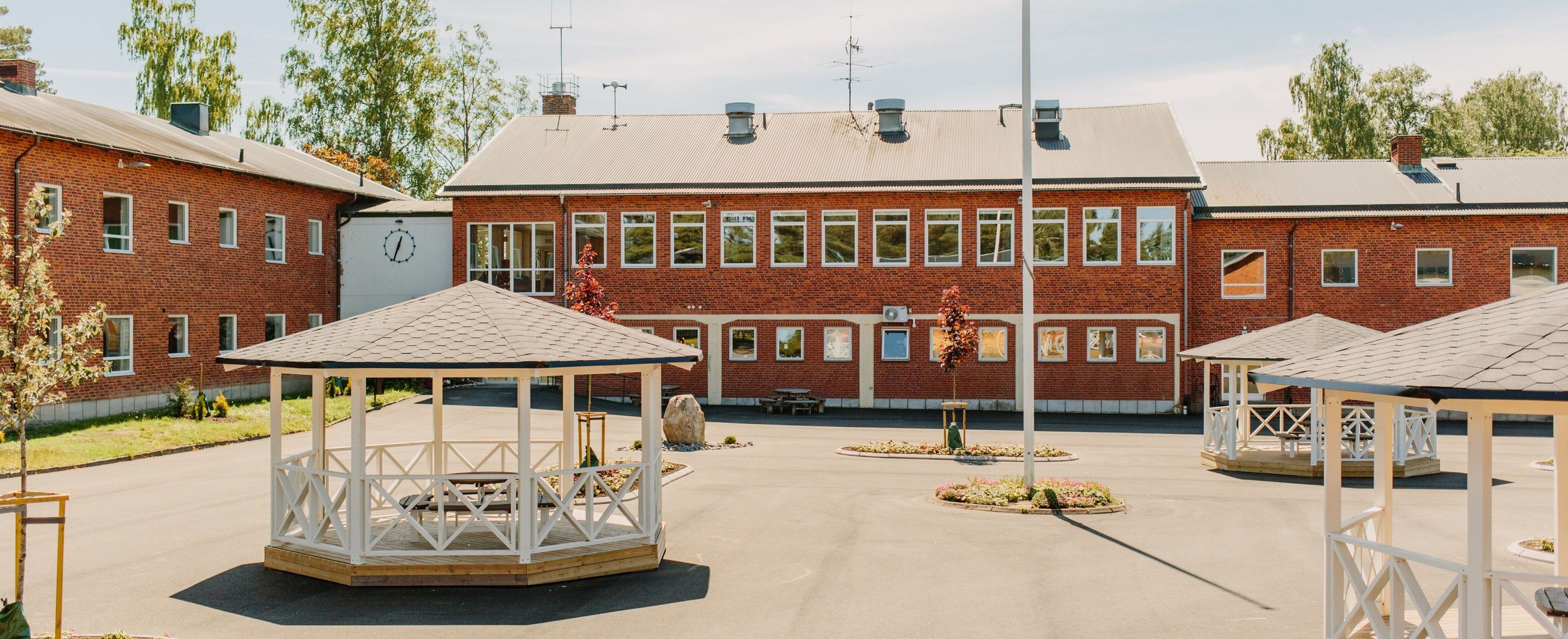 En röd tegelstensbyggnad med träd i höstfärger utanför. Det klättrar en buske upp för fasaden.